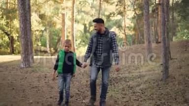 关爱的父亲在阳光明媚的秋日和他的孩子在森林里徒步旅行，男人和男孩牵着手走路和说话